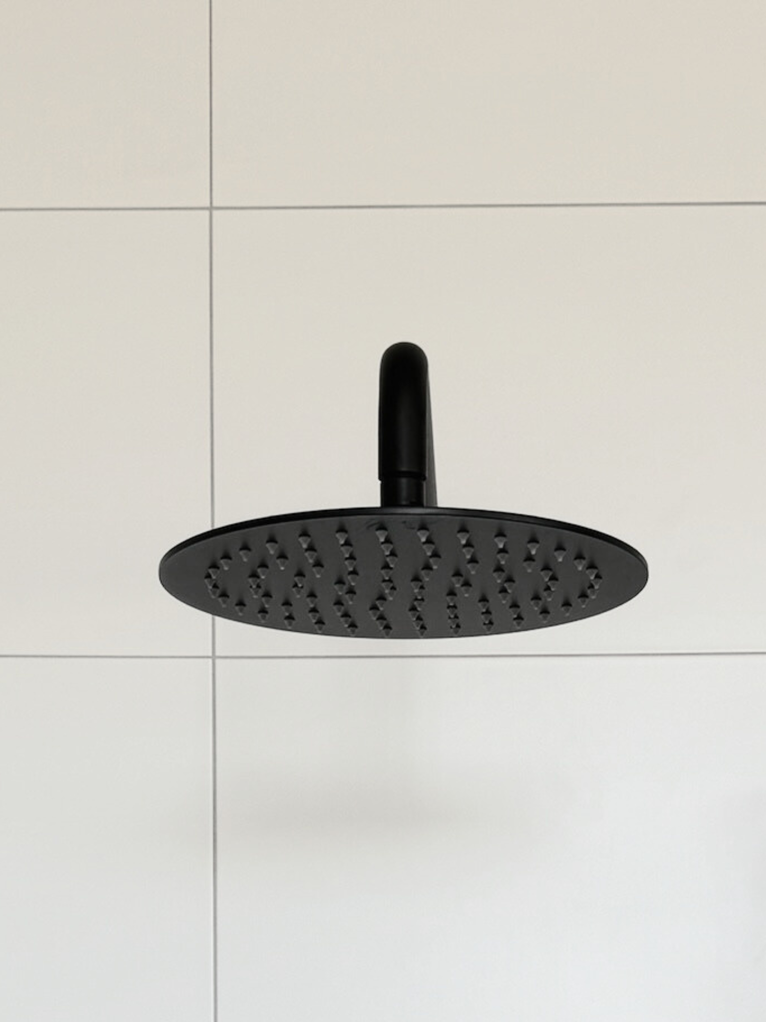 A black rain shower head with white tiles
